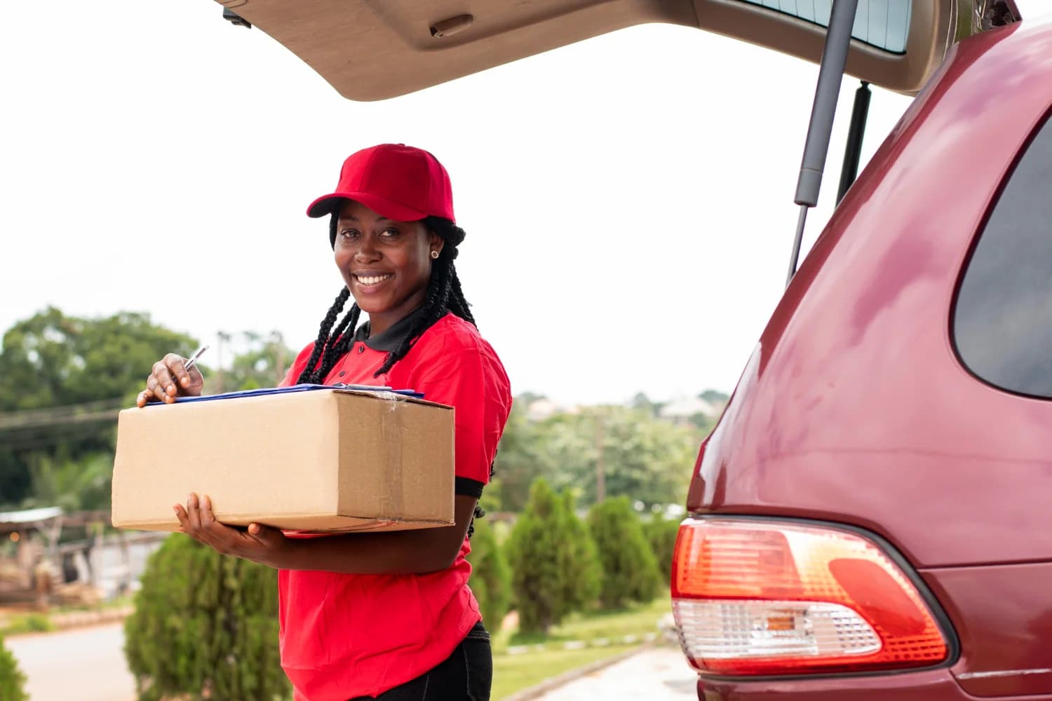 Delivery worker in a red uniform holding a parcel beside an open vehicle