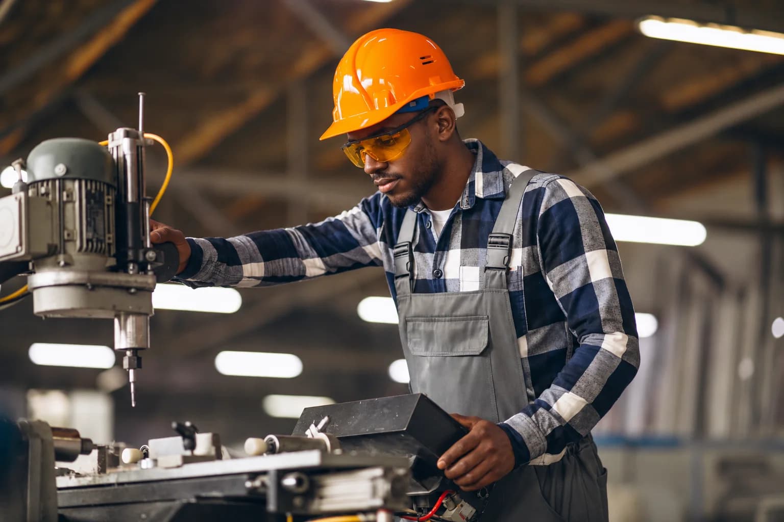 Black machinery operator wearing a hard hat and safety glasses in a workshop